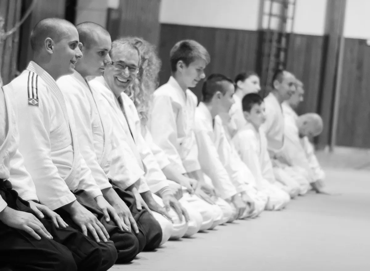 Usmiati cvičenci, dospelí aj deti, sedia v rade v seiza na tatami